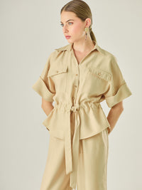Blusa tipo camisera con manga corta amplia, bolsillos frontales y ajuste en la cintura con lazo para definir la silueta. Su diseño estructurado y moderno combina funcionalidad y estilo, ideal para lograr un look casual con un aire sofisticado.

Detalles:

Color: Camel