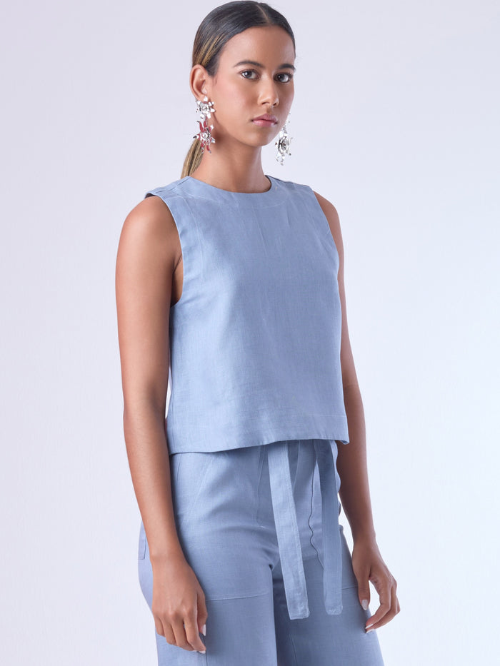 Blusa sin mangas de corte recto y silueta relajada. Tiene cuello redondo cerrado y un diseño limpio sin detalles visibles, lo que le da un estilo minimalista y moderno. El largo llega justo a la cintura, ideal para llevar por fuera o combinada con prendas de talle alto para un look fresco y sofisticado