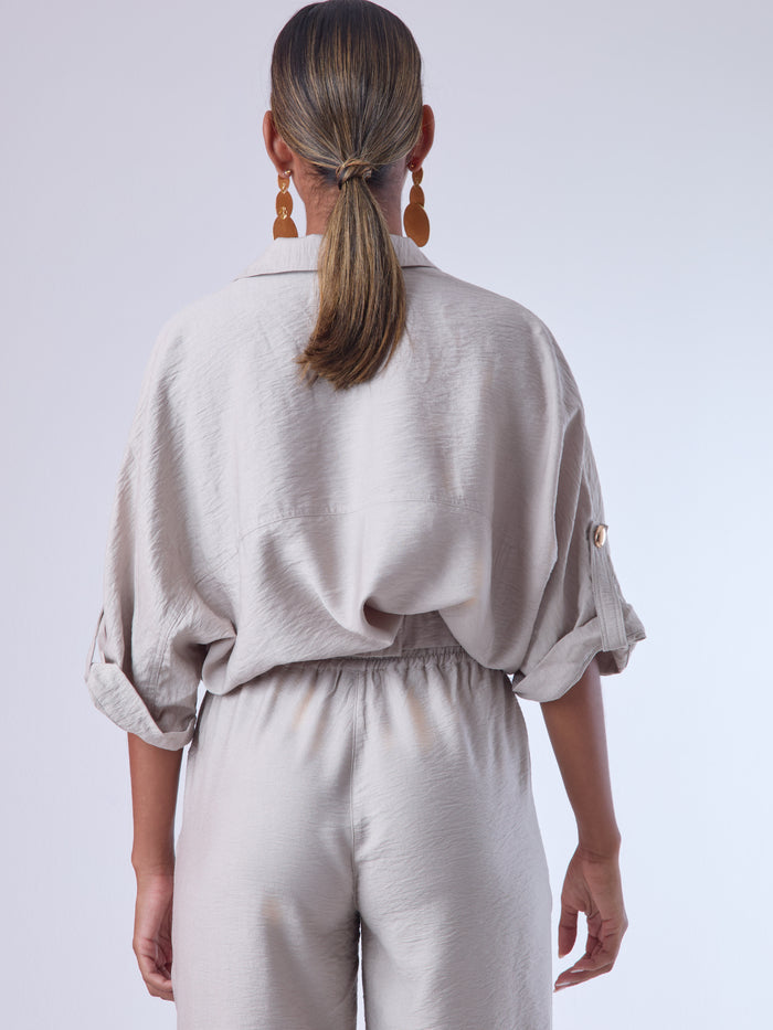 Relajada pero estructurada, esta blusa de silueta amplia combina un diseño utilitario con detalles refinados. Presenta bolsillos de solapa en el pecho, mangas con opción de ajuste y una botonadura dorada que aporta un toque de brillo sutil. Ideal para estilismos casuales con elegancia natural, o para elevar conjuntos relajados con una prenda clave y atemporal.
