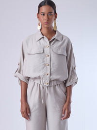 Relajada pero estructurada, esta blusa de silueta amplia combina un diseño utilitario con detalles refinados. Presenta bolsillos de solapa en el pecho, mangas con opción de ajuste y una botonadura dorada que aporta un toque de brillo sutil. Ideal para estilismos casuales con elegancia natural, o para elevar conjuntos relajados con una prenda clave y atemporal.