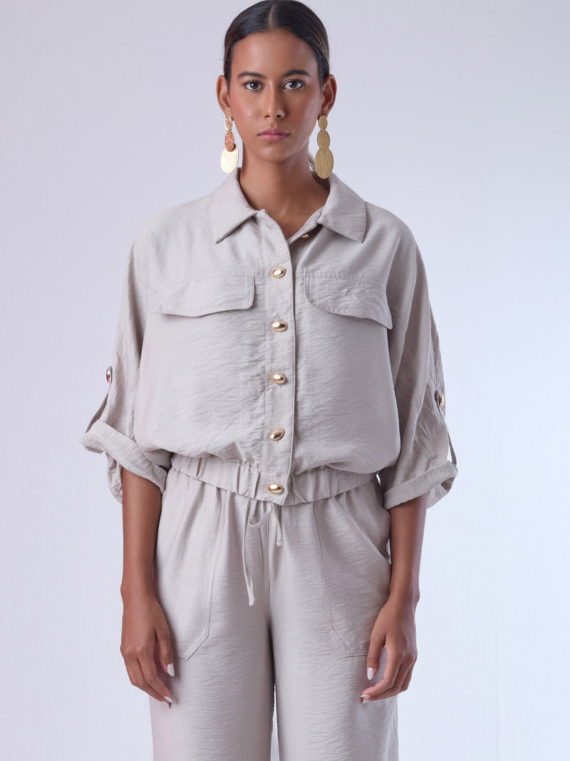 Relajada pero estructurada, esta blusa de silueta amplia combina un diseño utilitario con detalles refinados. Presenta bolsillos de solapa en el pecho, mangas con opción de ajuste y una botonadura dorada que aporta un toque de brillo sutil. Ideal para estilismos casuales con elegancia natural, o para elevar conjuntos relajados con una prenda clave y atemporal.