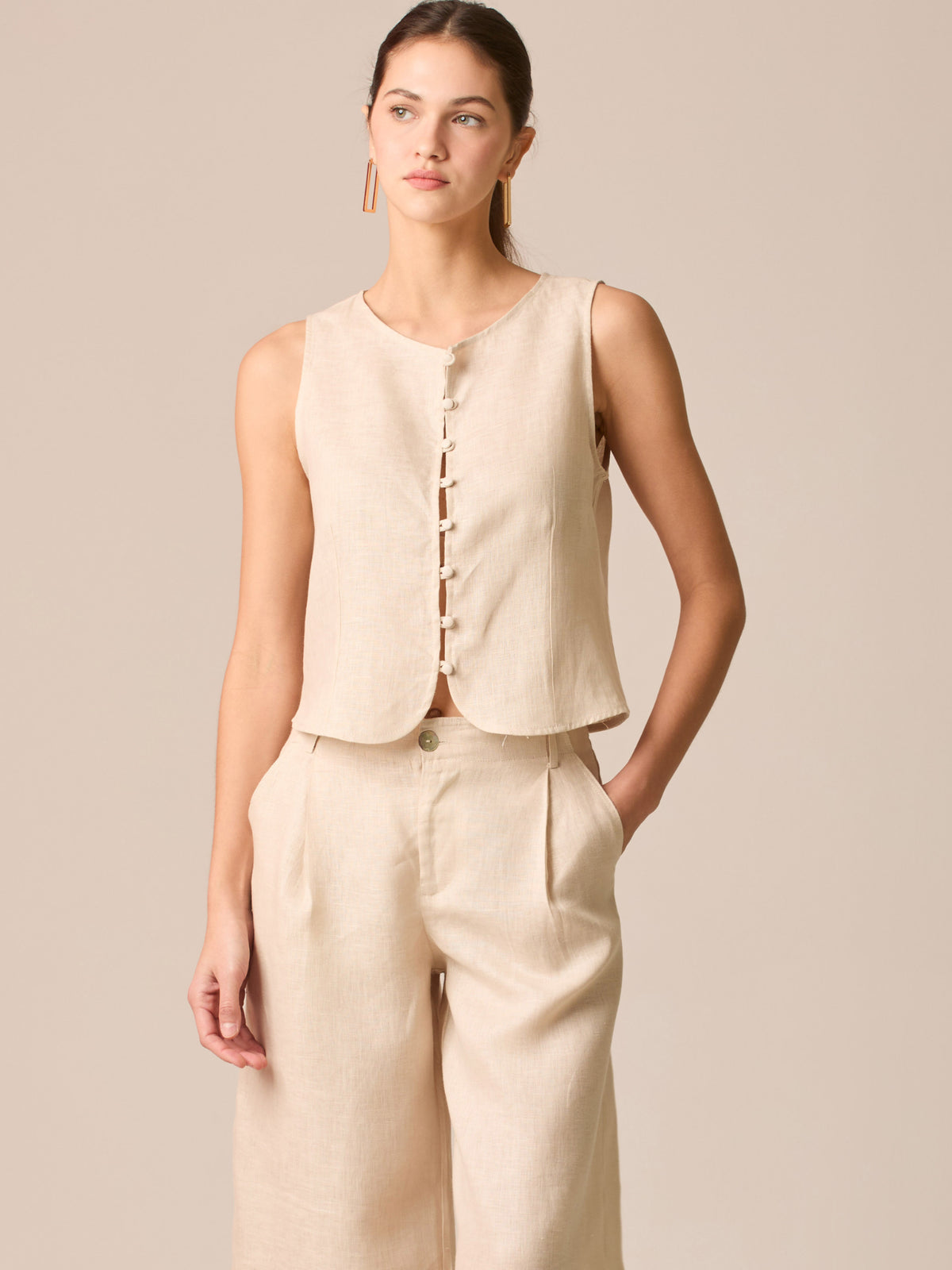 Blusa tipo chaleco sin mangas, con escote redondo y cierre frontal de botones forrados, entallada en la parte superior y con dobladillo ligeramente curvado que aporta un acabado elegante y estructurado