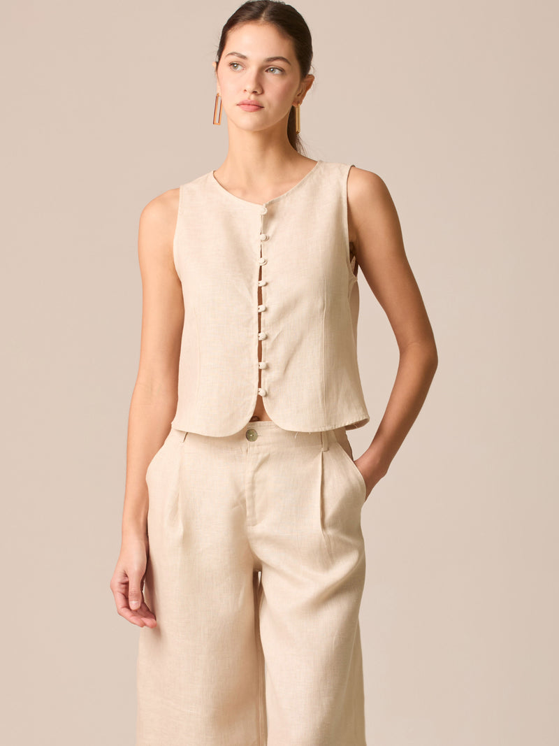 Blusa tipo chaleco sin mangas, con escote redondo y cierre frontal de botones forrados, entallada en la parte superior y con dobladillo ligeramente curvado que aporta un acabado elegante y estructurado