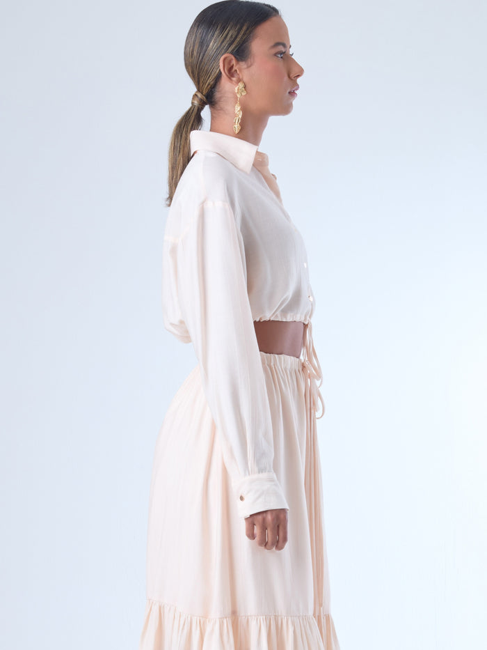 Blusa de corte relajado y largo cropped, con manga larga y puños con botones. Tiene cuello clásico camisero y una botonadura frontal. La prenda se ajusta a la cintura mediante un ligero fruncido con cordón interno, creando un efecto ablusado. Su estilo es casual con un toque sofisticado y femenino.

Detalles:

Color: Curuba

Material:18% Nylon 82% Rayón
