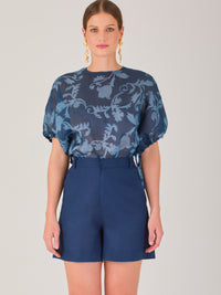 Blusa de manga corta con ajuste elástico en las mangas, corte recto y tejido semitransparente con diseño floral en relieve. Estilo elegante y ligero.