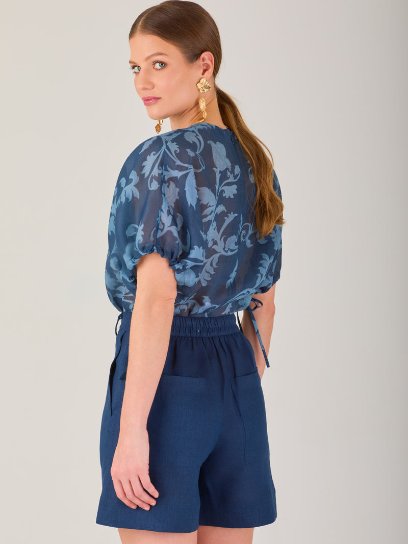 Blusa de manga corta con ajuste elástico en las mangas, corte recto y tejido semitransparente con diseño floral en relieve. Estilo elegante y ligero.