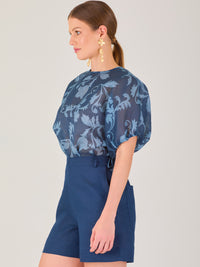 Blusa de manga corta con ajuste elástico en las mangas, corte recto y tejido semitransparente con diseño floral en relieve. Estilo elegante y ligero.