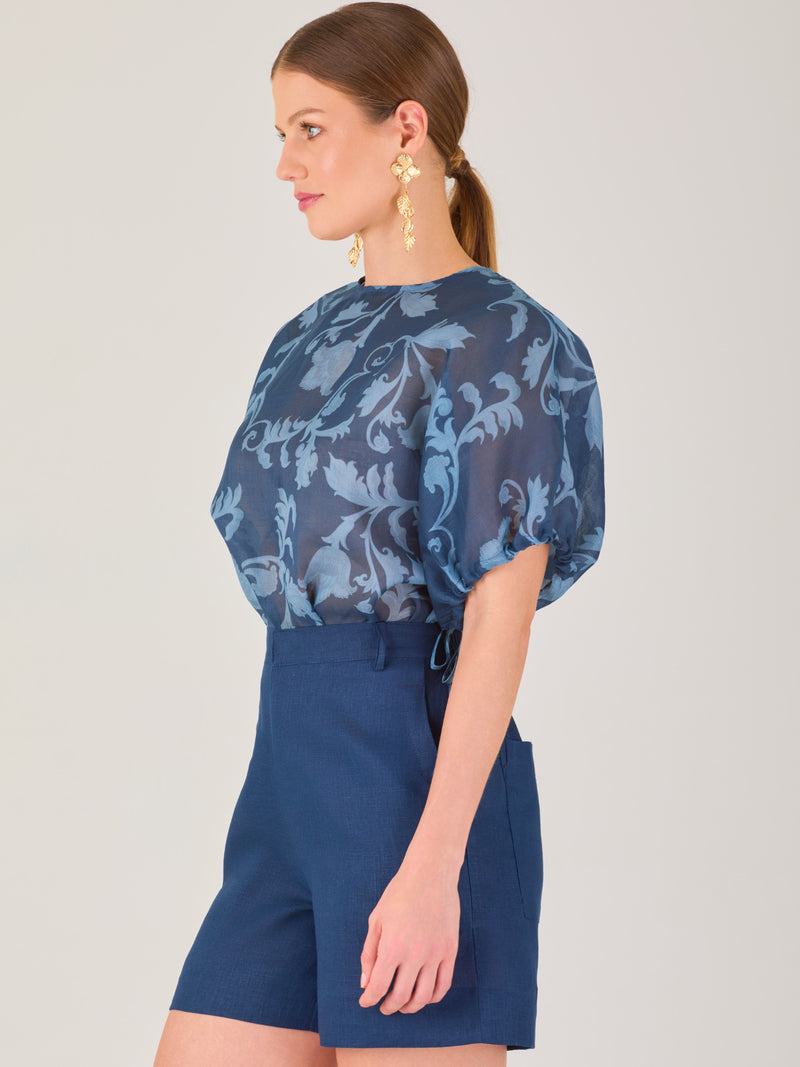Blusa de manga corta con ajuste elástico en las mangas, corte recto y tejido semitransparente con diseño floral en relieve. Estilo elegante y ligero.