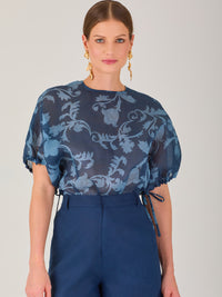 Blusa de manga corta con ajuste elástico en las mangas, corte recto y tejido semitransparente con diseño floral en relieve. Estilo elegante y ligero.