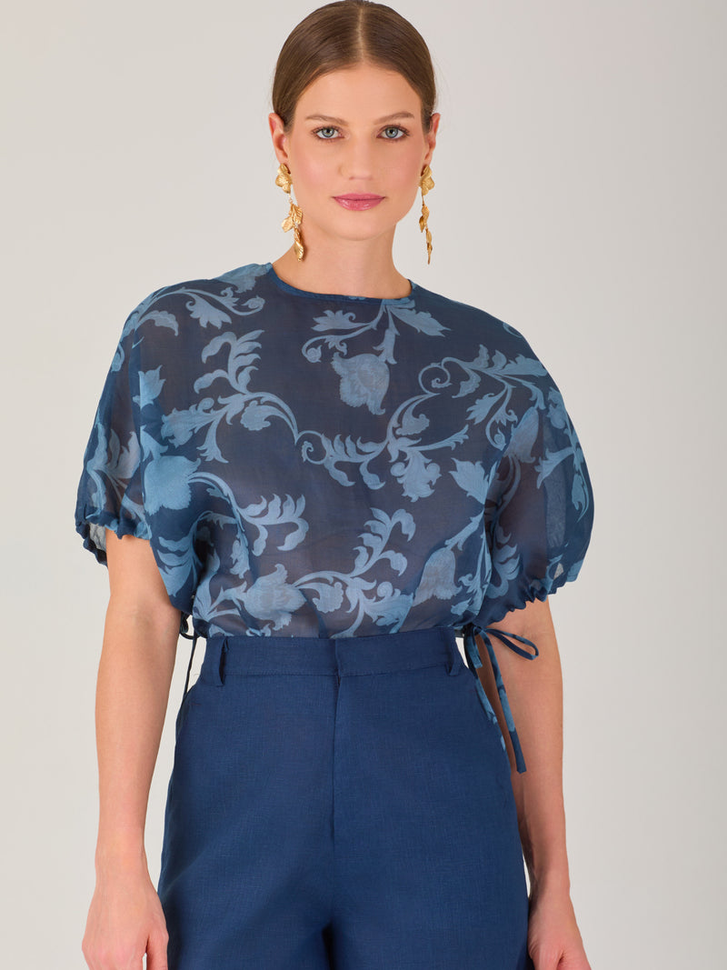Blusa de manga corta con ajuste elástico en las mangas, corte recto y tejido semitransparente con diseño floral en relieve. Estilo elegante y ligero.