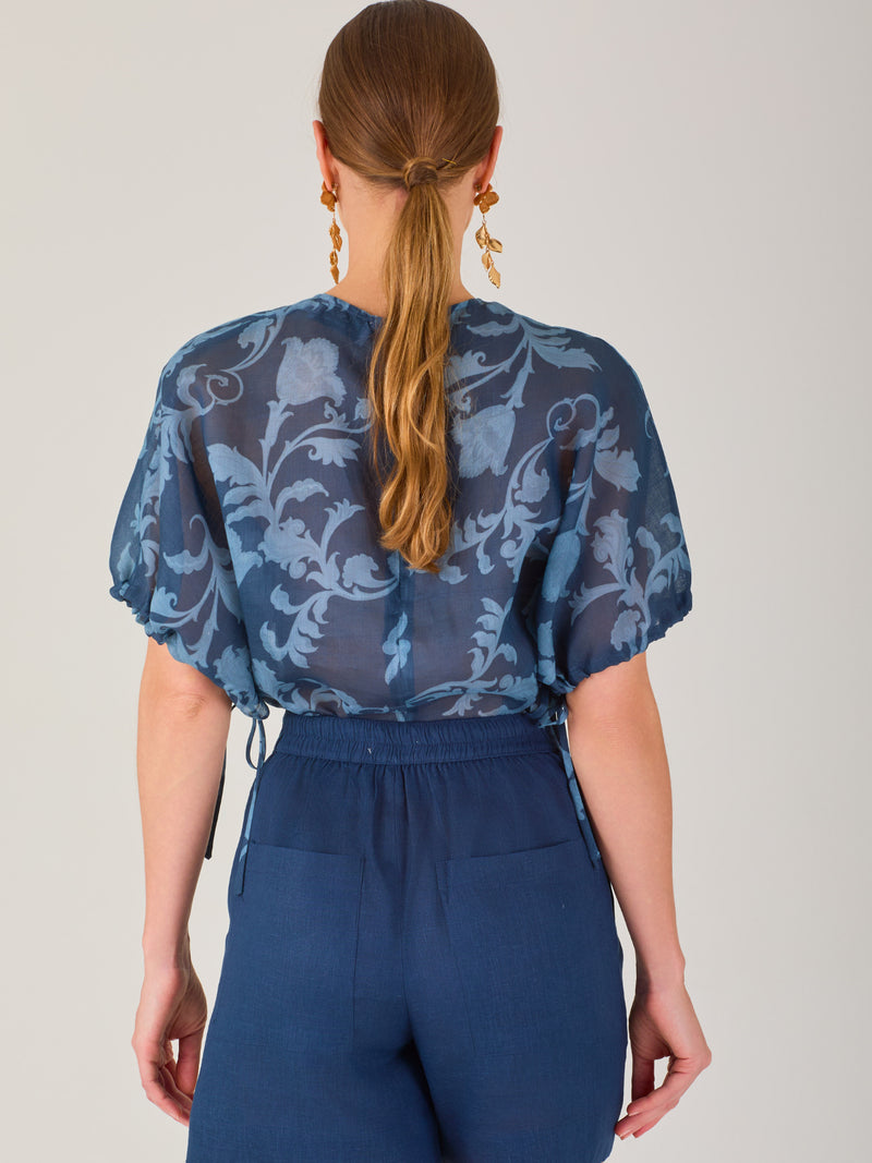 Blusa de manga corta con ajuste elástico en las mangas, corte recto y tejido semitransparente con diseño floral en relieve. Estilo elegante y ligero.