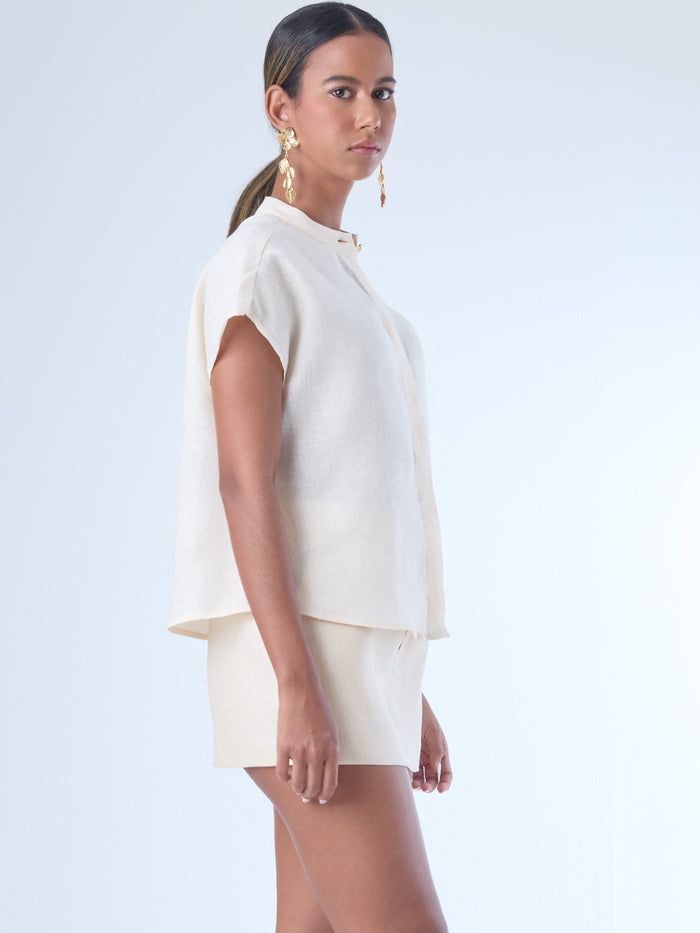Blusa de silueta recta con manga corta tipo caída y estructura relajada. Cuenta con cuello que se cierra con un pequeño broche metálico decorativos estilo sobrio la hace versátil y elegante, ideal para atuendos casuales o más refinados.