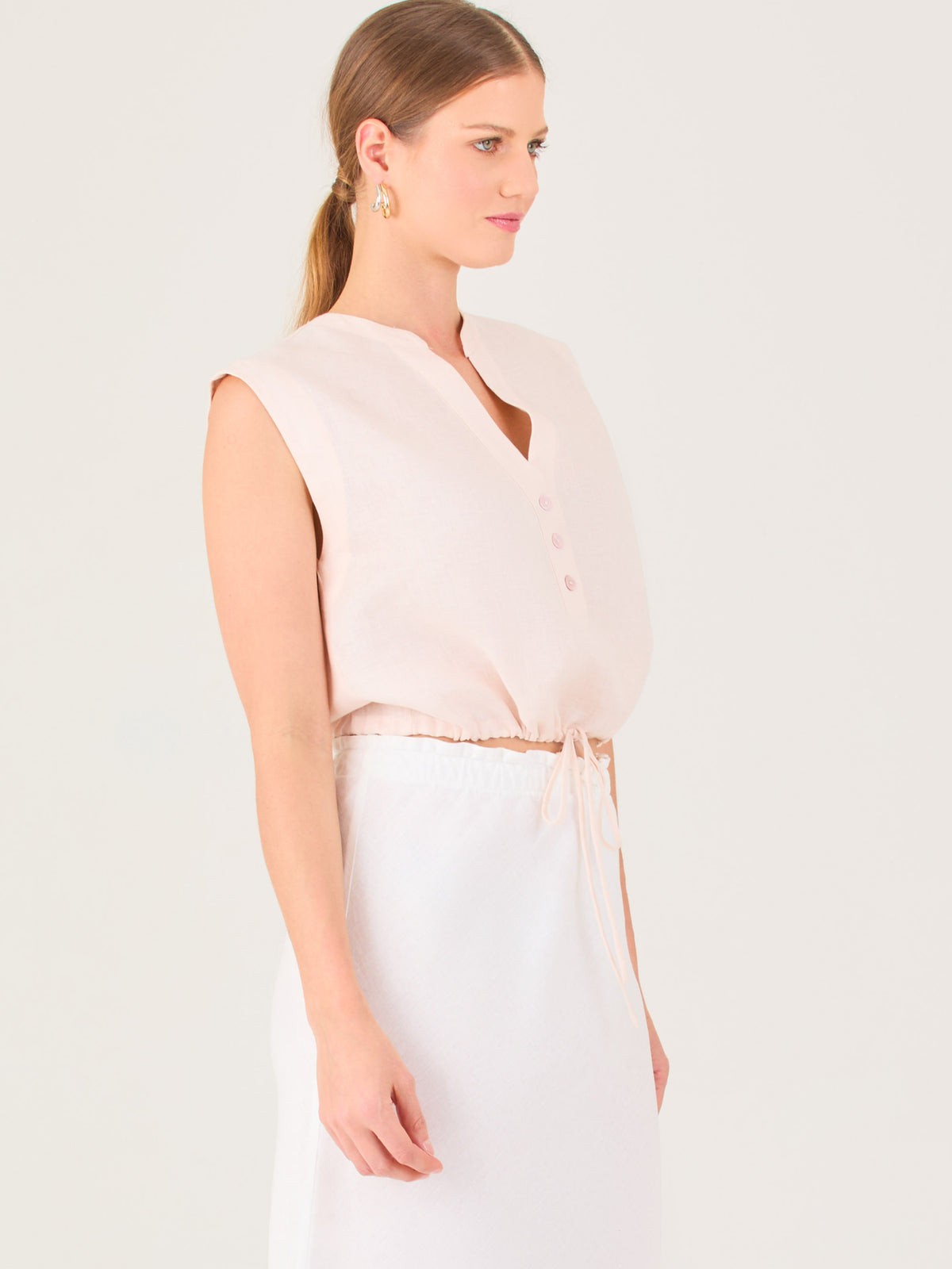 Blusa sin mangas con escote en V y botones frontales. Ajuste en la cintura con cordón, creando un efecto fruncido. Diseño ligero y femenino.

Detalles: