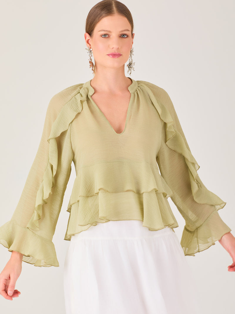 Ligera y romántica, esta blusa de textura vaporosa destaca por sus volantes en capas que aportan movimiento y fluidez. El escote en V y las mangas amplias con acabado ondulado añaden un toque delicado y sofisticado. Ideal para ocasiones especiales, cenas o estilismos casuales con un aire femenino y refinado.
