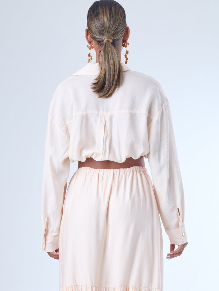 Blusa de corte relajado y largo cropped, con manga larga y puños con botones. Tiene cuello clásico camisero y una botonadura frontal. La prenda se ajusta a la cintura mediante un ligero fruncido con cordón interno, creando un efecto ablusado. Su estilo es casual con un toque sofisticado y femenino.

Detalles:

Color: Curuba

Material:18% Nylon 82% Rayón