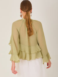Ligera y romántica, esta blusa de textura vaporosa destaca por sus volantes en capas que aportan movimiento y fluidez. El escote en V y las mangas amplias con acabado ondulado añaden un toque delicado y sofisticado. Ideal para ocasiones especiales, cenas o estilismos casuales con un aire femenino y refinado.