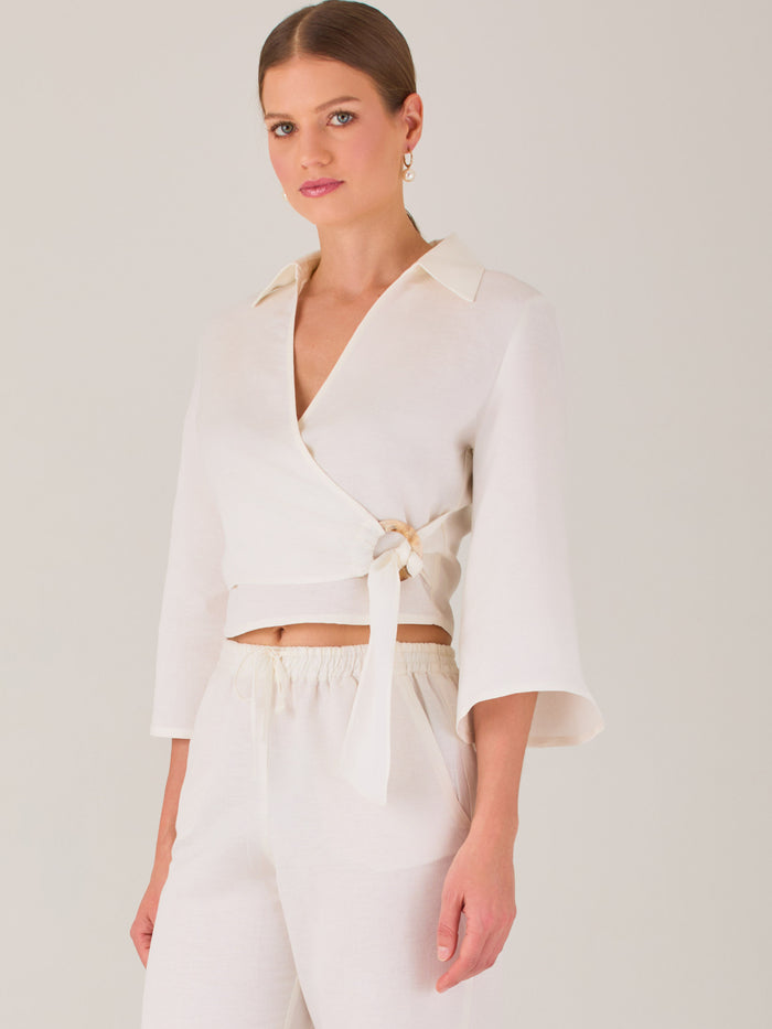 Blusa cruzada de manga tres cuartos y corte recto. Tiene cuello clásico y se ajusta con un lazo lateral que añade un toque elegante y moderno.

Detalles:

Color: Blanco

Material: 52% Lino 48% Rayón