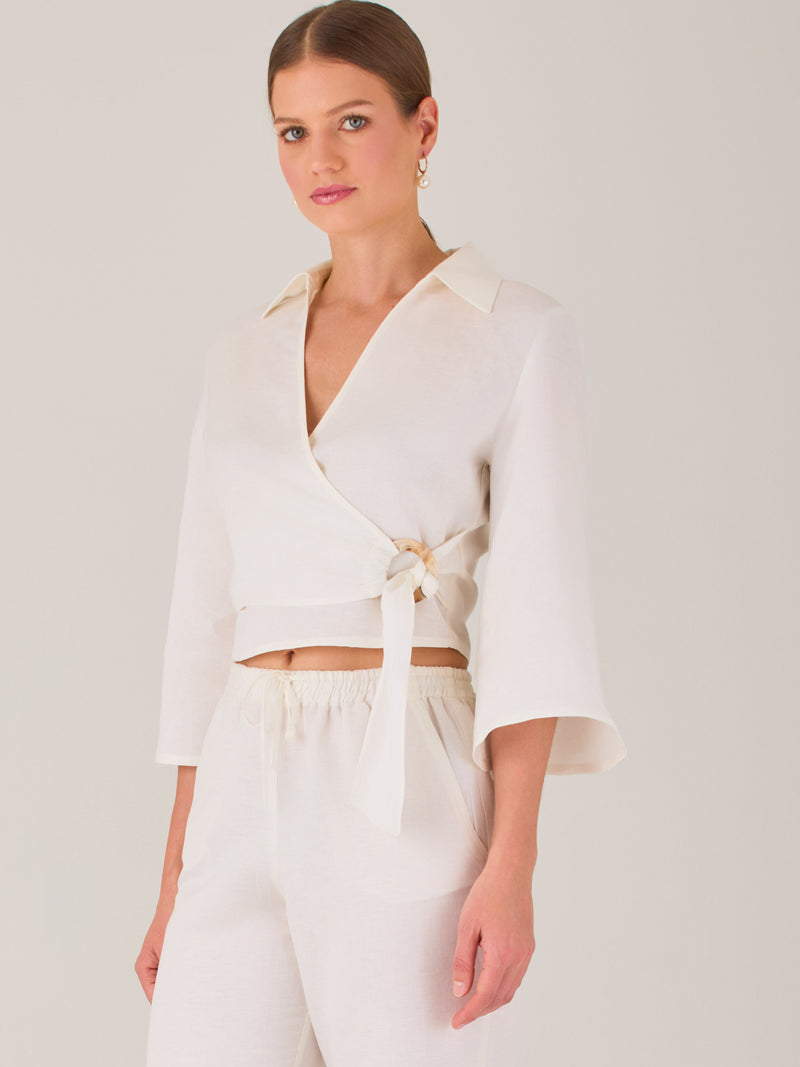 Blusa cruzada de manga tres cuartos y corte recto. Tiene cuello clásico y se ajusta con un lazo lateral que añade un toque elegante y moderno.

Detalles:

Color: Blanco

Material: 52% Lino 48% Rayón