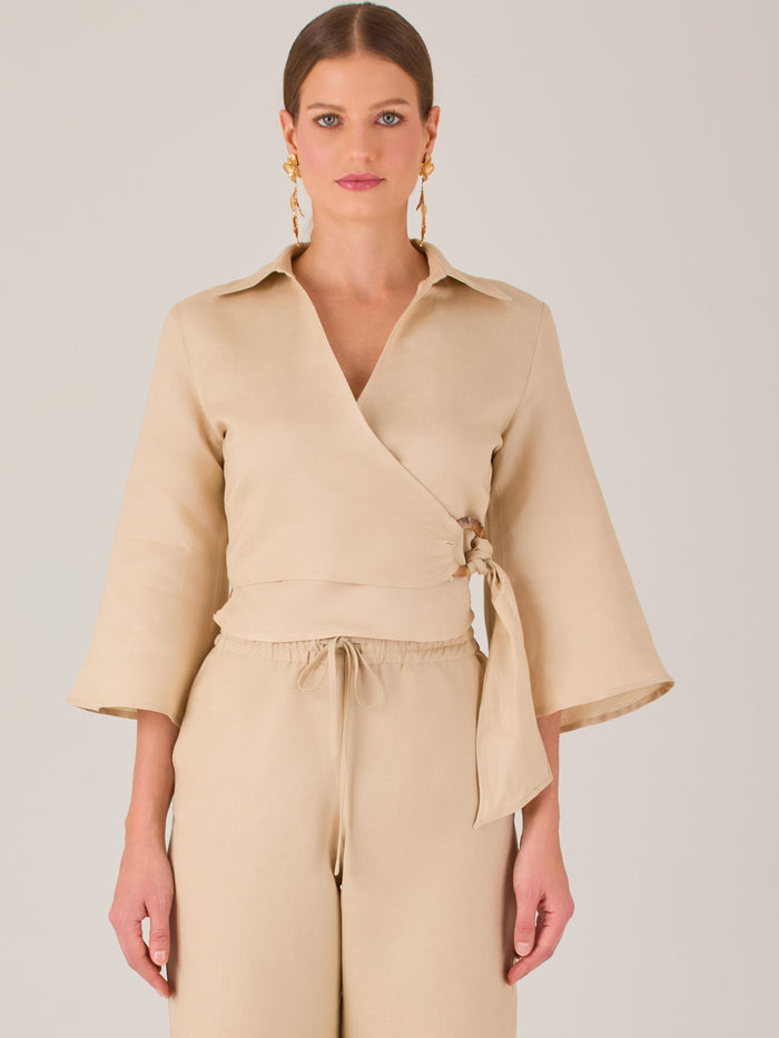 Blusa cruzada de manga tres cuartos y corte recto. Tiene cuello clásico y se ajusta con un lazo lateral que añade un toque elegante y moderno.