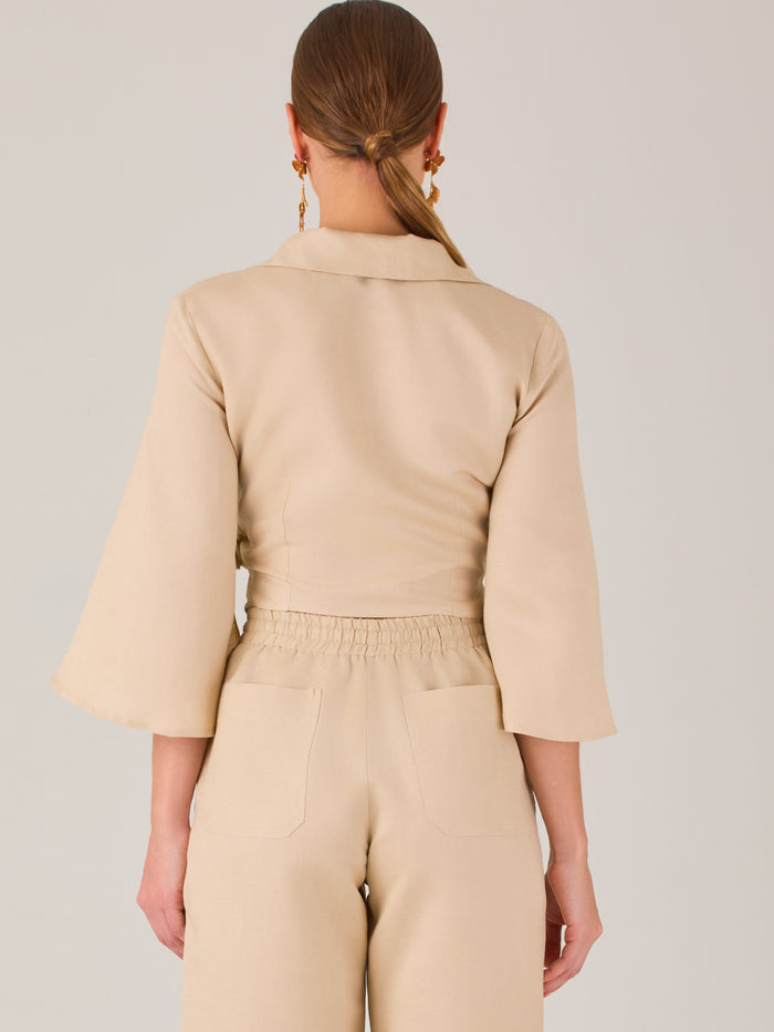Blusa cruzada de manga tres cuartos y corte recto. Tiene cuello clásico y se ajusta con un lazo lateral que añade un toque elegante y moderno.