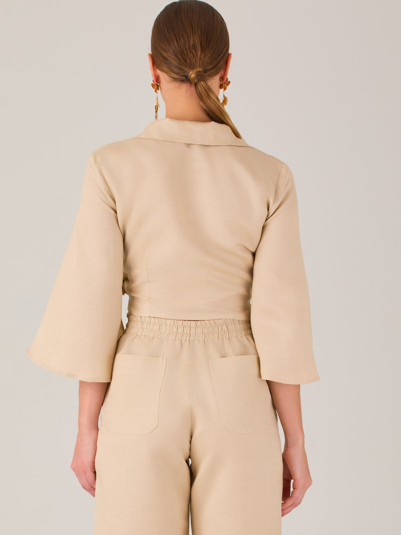Blusa cruzada de manga tres cuartos y corte recto. Tiene cuello clásico y se ajusta con un lazo lateral que añade un toque elegante y moderno.