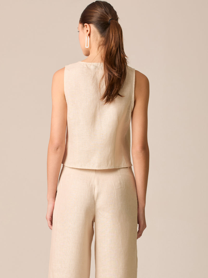 Blusa tipo chaleco sin mangas, con escote redondo y cierre frontal de botones forrados, entallada en la parte superior y con dobladillo ligeramente curvado que aporta un acabado elegante y estructurado
