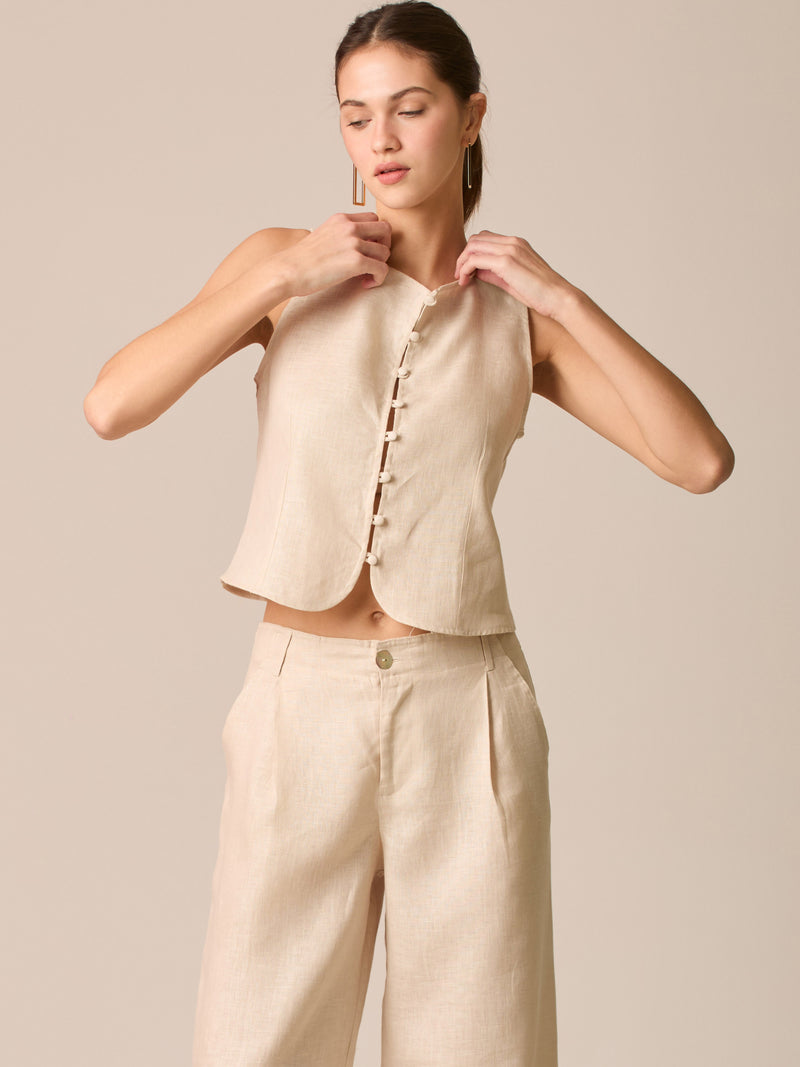 Blusa tipo chaleco sin mangas, con escote redondo y cierre frontal de botones forrados, entallada en la parte superior y con dobladillo ligeramente curvado que aporta un acabado elegante y estructurado