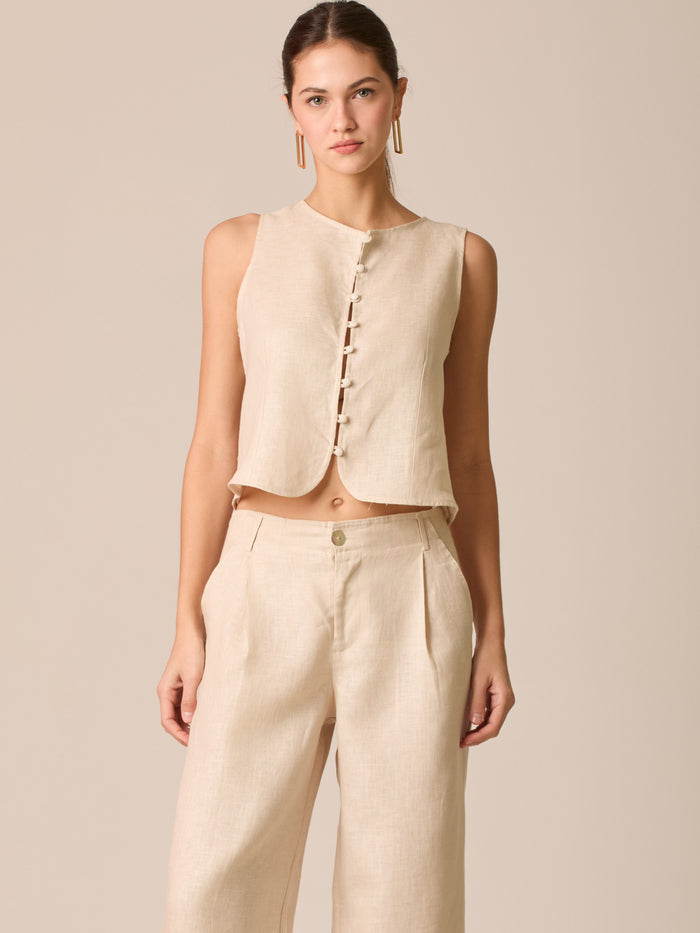 Blusa tipo chaleco sin mangas, con escote redondo y cierre frontal de botones forrados, entallada en la parte superior y con dobladillo ligeramente curvado que aporta un acabado elegante y estructurado