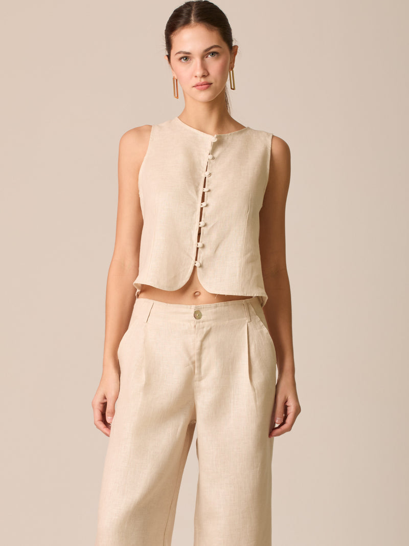 Blusa tipo chaleco sin mangas, con escote redondo y cierre frontal de botones forrados, entallada en la parte superior y con dobladillo ligeramente curvado que aporta un acabado elegante y estructurado