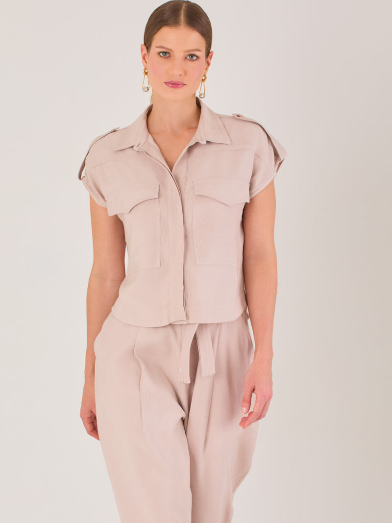 Blusa blanca de estilo camisero con un diseño moderno y minimalista. Cuenta con cuello clásico, tapeta oculta para los botones y mangas cortas tipo caída con detalle de charreteras en los hombros. Posee dos bolsillos de parche en el pecho que le aportan un toque utilitario y estructurado. Su corte recto y fluido la hace ideal tanto para looks casuales como elegantes