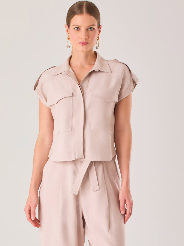 Blusa blanca de estilo camisero con un diseño moderno y minimalista. Cuenta con cuello clásico, tapeta oculta para los botones y mangas cortas tipo caída con detalle de charreteras en los hombros. Posee dos bolsillos de parche en el pecho que le aportan un toque utilitario y estructurado. Su corte recto y fluido la hace ideal tanto para looks casuales como elegantes