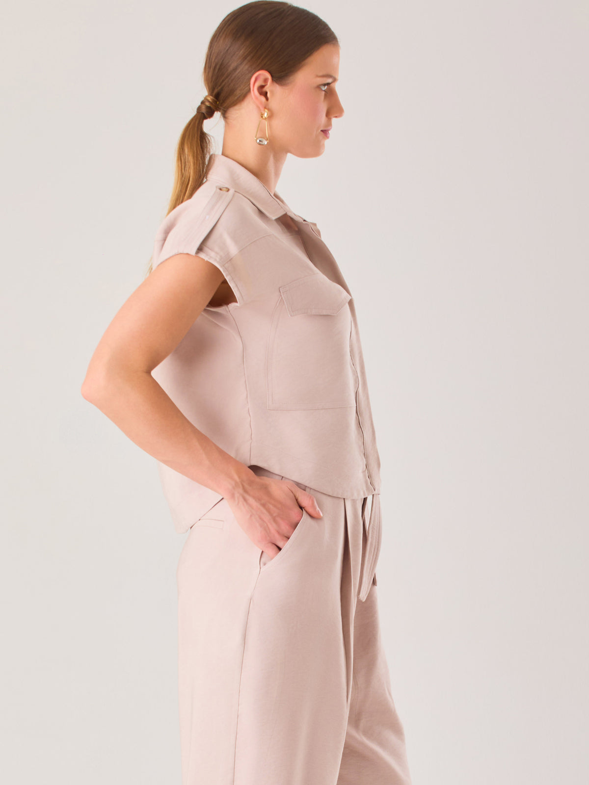 Blusa blanca de estilo camisero con un diseño moderno y minimalista. Cuenta con cuello clásico, tapeta oculta para los botones y mangas cortas tipo caída con detalle de charreteras en los hombros. Posee dos bolsillos de parche en el pecho que le aportan un toque utilitario y estructurado. Su corte recto y fluido la hace ideal tanto para looks casuales como elegantes