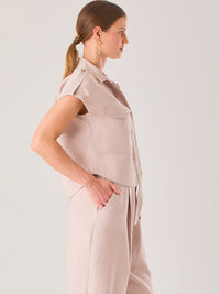 Blusa blanca de estilo camisero con un diseño moderno y minimalista. Cuenta con cuello clásico, tapeta oculta para los botones y mangas cortas tipo caída con detalle de charreteras en los hombros. Posee dos bolsillos de parche en el pecho que le aportan un toque utilitario y estructurado. Su corte recto y fluido la hace ideal tanto para looks casuales como elegantes