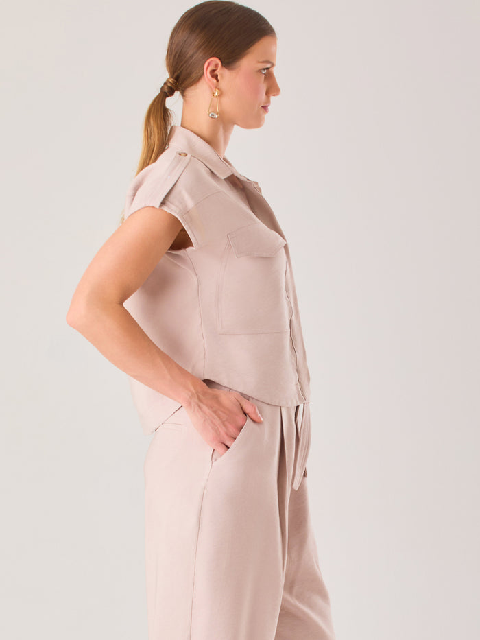 Blusa blanca de estilo camisero con un diseño moderno y minimalista. Cuenta con cuello clásico, tapeta oculta para los botones y mangas cortas tipo caída con detalle de charreteras en los hombros. Posee dos bolsillos de parche en el pecho que le aportan un toque utilitario y estructurado. Su corte recto y fluido la hace ideal tanto para looks casuales como elegantes