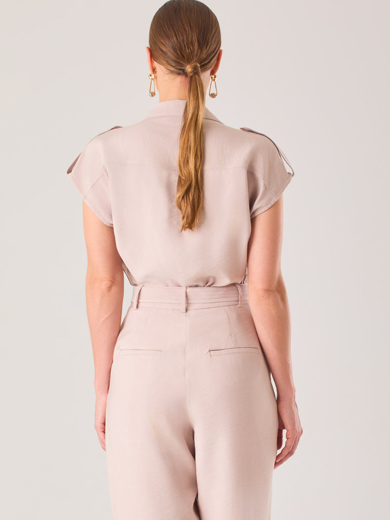 Blusa blanca de estilo camisero con un diseño moderno y minimalista. Cuenta con cuello clásico, tapeta oculta para los botones y mangas cortas tipo caída con detalle de charreteras en los hombros. Posee dos bolsillos de parche en el pecho que le aportan un toque utilitario y estructurado. Su corte recto y fluido la hace ideal tanto para looks casuales como elegantes