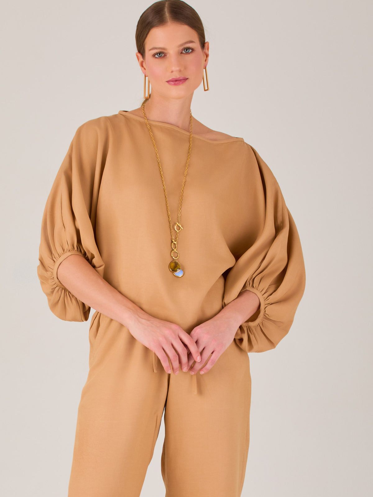 Con un diseño sobrio y sofisticado, esta blusa se distingue por su silueta recta y mangas globo tres cuartos con puño ajustado. El escote recto y el tejido con cuerpo le dan un aire minimalista ideal para combinar con pantalones de sastre o faldas estructuradas. Perfecta para elevar looks formales o casuales con discreta elegancia.