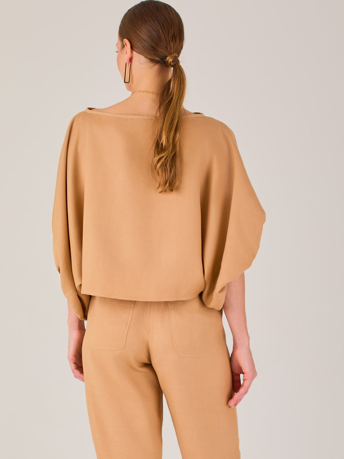 Con un diseño sobrio y sofisticado, esta blusa se distingue por su silueta recta y mangas globo tres cuartos con puño ajustado. El escote recto y el tejido con cuerpo le dan un aire minimalista ideal para combinar con pantalones de sastre o faldas estructuradas. Perfecta para elevar looks formales o casuales con discreta elegancia.
