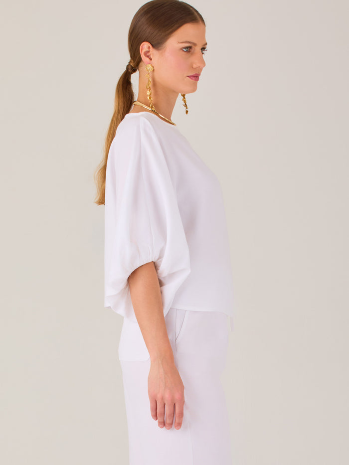 Sofisticada y atemporal, esta blusa de silueta recta se caracteriza por su escote cerrado, líneas limpias y mangas tres cuartos con efecto globo. El diseño pulido la convierte en una prenda versátil para combinar con prendas sastre o looks relajados, ideal para ambientes laborales o estilismos casuales con elegancia natural.