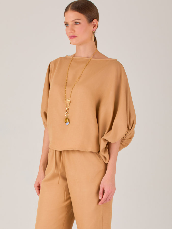 Con un diseño sobrio y sofisticado, esta blusa se distingue por su silueta recta y mangas globo tres cuartos con puño ajustado. El escote recto y el tejido con cuerpo le dan un aire minimalista ideal para combinar con pantalones de sastre o faldas estructuradas. Perfecta para elevar looks formales o casuales con discreta elegancia.