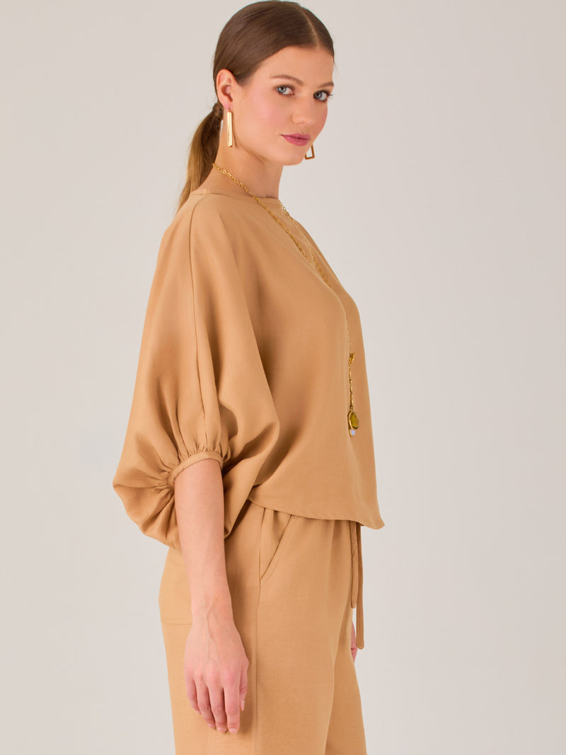Con un diseño sobrio y sofisticado, esta blusa se distingue por su silueta recta y mangas globo tres cuartos con puño ajustado. El escote recto y el tejido con cuerpo le dan un aire minimalista ideal para combinar con pantalones de sastre o faldas estructuradas. Perfecta para elevar looks formales o casuales con discreta elegancia.