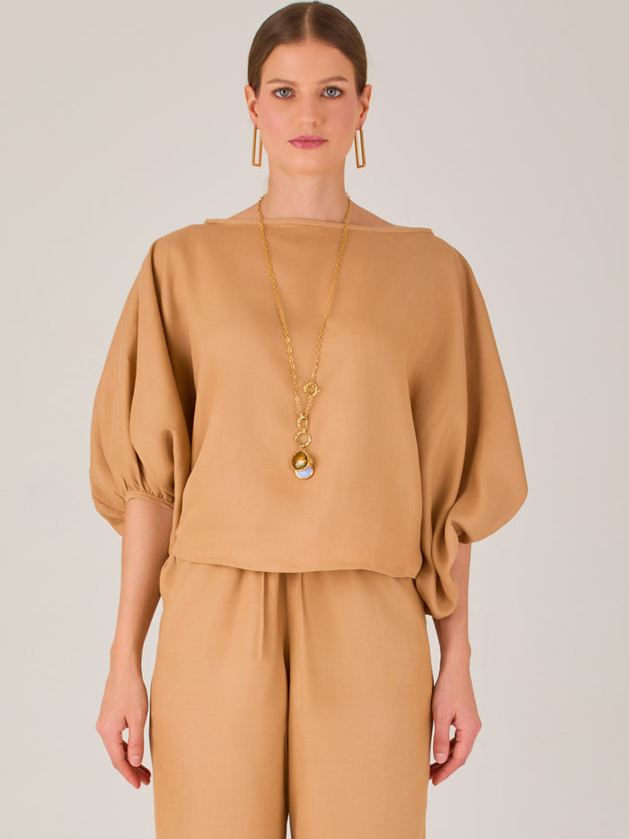 Con un diseño sobrio y sofisticado, esta blusa se distingue por su silueta recta y mangas globo tres cuartos con puño ajustado. El escote recto y el tejido con cuerpo le dan un aire minimalista ideal para combinar con pantalones de sastre o faldas estructuradas. Perfecta para elevar looks formales o casuales con discreta elegancia.