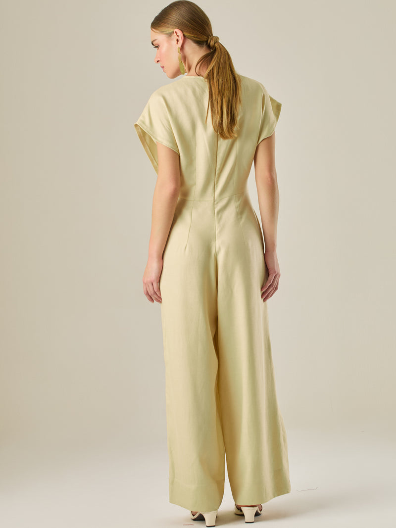 Este enterizo presenta un diseño elegante y minimalista, ideal para ocasiones casuales con estilo o eventos diurnos sofisticados. Confeccionado en un tono beige claro, tiene un corte relajado con mangas tipo kimono, cuello redondo y un diseño limpio sin botones ni cierres visibles en el frente. La prenda se ajusta en la cintura con un cinturón del mismo tejido, que se anuda al frente, creando una silueta favorecedora. El pantalón es de pierna ancha y caída fluida, lo que aporta comodidad y movimiento. Compl