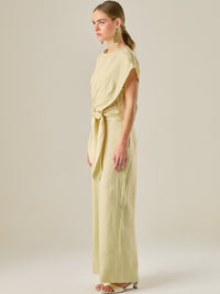 Este enterizo presenta un diseño elegante y minimalista, ideal para ocasiones casuales con estilo o eventos diurnos sofisticados. Confeccionado en un tono beige claro, tiene un corte relajado con mangas tipo kimono, cuello redondo y un diseño limpio sin botones ni cierres visibles en el frente. La prenda se ajusta en la cintura con un cinturón del mismo tejido, que se anuda al frente, creando una silueta favorecedora. El pantalón es de pierna ancha y caída fluida, lo que aporta comodidad y movimiento. Compl