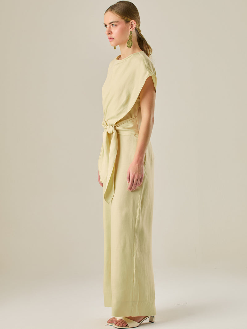 Este enterizo presenta un diseño elegante y minimalista, ideal para ocasiones casuales con estilo o eventos diurnos sofisticados. Confeccionado en un tono beige claro, tiene un corte relajado con mangas tipo kimono, cuello redondo y un diseño limpio sin botones ni cierres visibles en el frente. La prenda se ajusta en la cintura con un cinturón del mismo tejido, que se anuda al frente, creando una silueta favorecedora. El pantalón es de pierna ancha y caída fluida, lo que aporta comodidad y movimiento. Compl