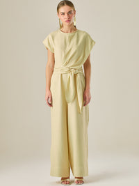Este enterizo presenta un diseño elegante y minimalista, ideal para ocasiones casuales con estilo o eventos diurnos sofisticados. Confeccionado en un tono beige claro, tiene un corte relajado con mangas tipo kimono, cuello redondo y un diseño limpio sin botones ni cierres visibles en el frente. La prenda se ajusta en la cintura con un cinturón del mismo tejido, que se anuda al frente, creando una silueta favorecedora. El pantalón es de pierna ancha y caída fluida, lo que aporta comodidad y movimiento. Compl
