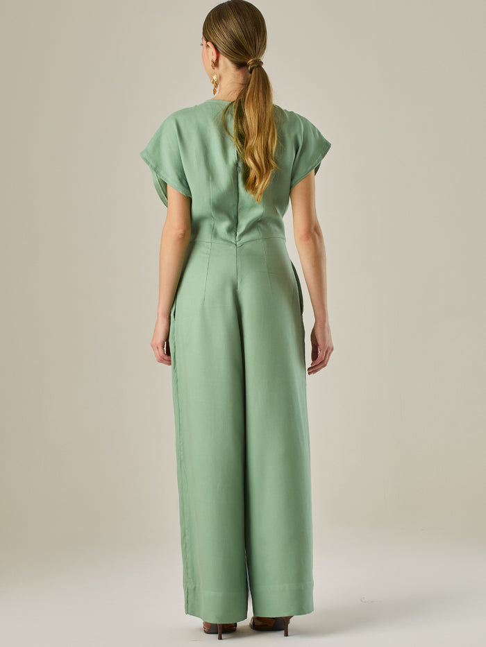 Este enterizo presenta un diseño elegante y minimalista, ideal para ocasiones casuales con estilo o eventos diurnos sofisticados. Confeccionado en un tono beige claro, tiene un corte relajado con mangas tipo kimono, cuello redondo y un diseño limpio sin botones ni cierres visibles en el frente. La prenda se ajusta en la cintura con un cinturón del mismo tejido, que se anuda al frente, creando una silueta favorecedora. El pantalón es de pierna ancha y caída fluida, lo que aporta comodidad y movimiento. Compl
