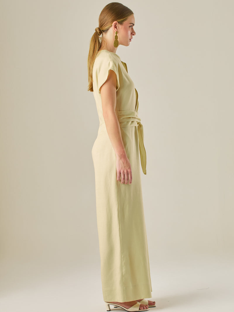 Este enterizo presenta un diseño elegante y minimalista, ideal para ocasiones casuales con estilo o eventos diurnos sofisticados. Confeccionado en un tono beige claro, tiene un corte relajado con mangas tipo kimono, cuello redondo y un diseño limpio sin botones ni cierres visibles en el frente. La prenda se ajusta en la cintura con un cinturón del mismo tejido, que se anuda al frente, creando una silueta favorecedora. El pantalón es de pierna ancha y caída fluida, lo que aporta comodidad y movimiento. Compl
