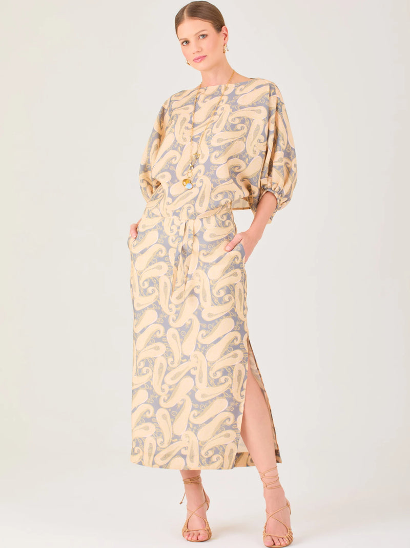 La falda es de corte largo y recto, con una abertura lateral que aporta movimiento y frescura. Presenta un diseño de estampado integral con figuras orgánicas curvas que se repiten en todo el tejido. El estilo es relajado pero elegante, con bolsillos laterales que le añaden funcionalidad y un ajuste cómodo a la cintura