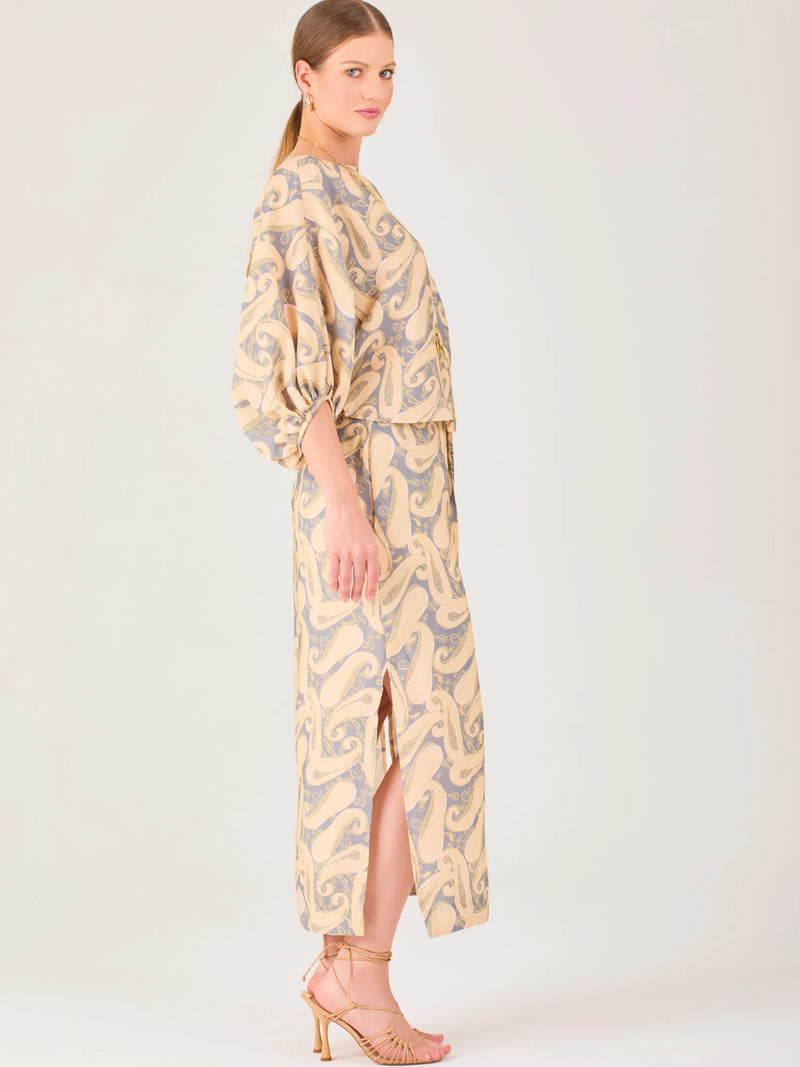 La falda es de corte largo y recto, con una abertura lateral que aporta movimiento y frescura. Presenta un diseño de estampado integral con figuras orgánicas curvas que se repiten en todo el tejido. El estilo es relajado pero elegante, con bolsillos laterales que le añaden funcionalidad y un ajuste cómodo a la cintura