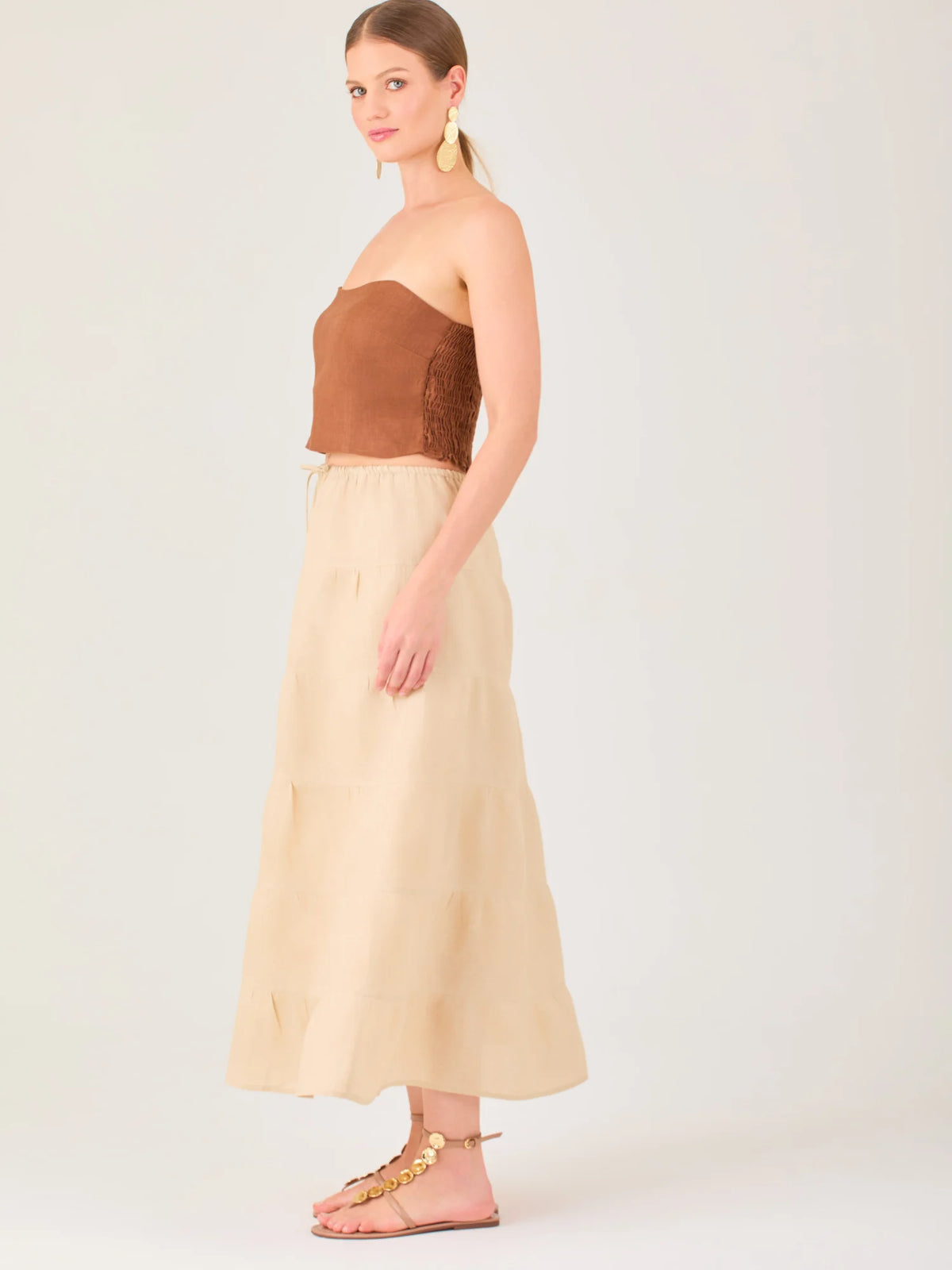 La falda es de largo midi, confeccionada en una tela ligera de tono beige claro. Presenta un diseño de corte amplio con caída fluida y detalles de costuras horizontales que crean un efecto de franjas sutiles a lo largo de la prenda. La pretina es elástica con cordón ajustable al frente, lo que le aporta comodidad y un estilo relajado. Su diseño minimalista y neutral la hace versátil, ideal para combinar con diferentes tops y accesorios, manteniendo un aire fresco y natural.